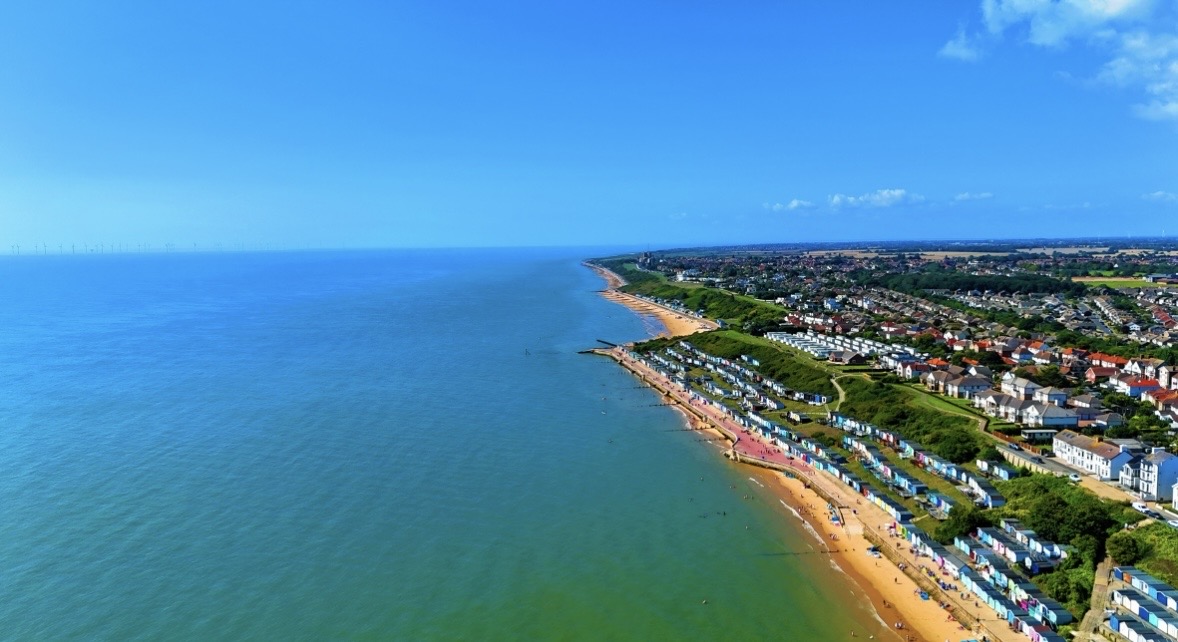 Sweeping aerial view of a coastline, beach huts and seaside town
