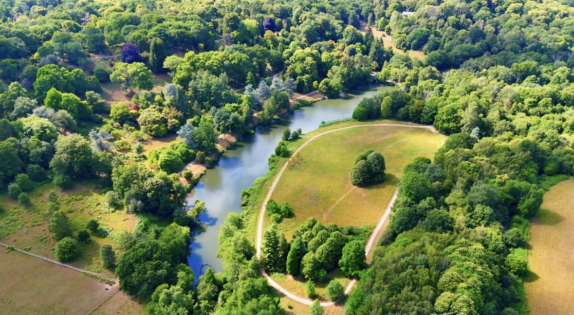 Aerial view across green parkland with a winding lake and woodland